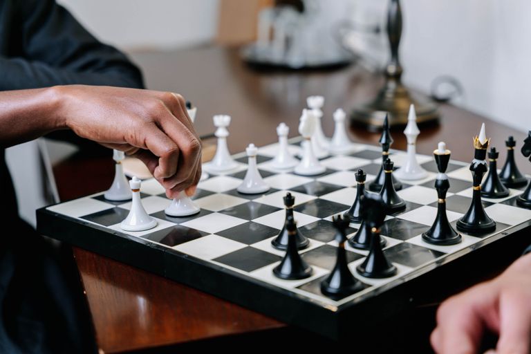 Close-up of a chessboard during a game, featuring a hand moving chess pieces strategically.