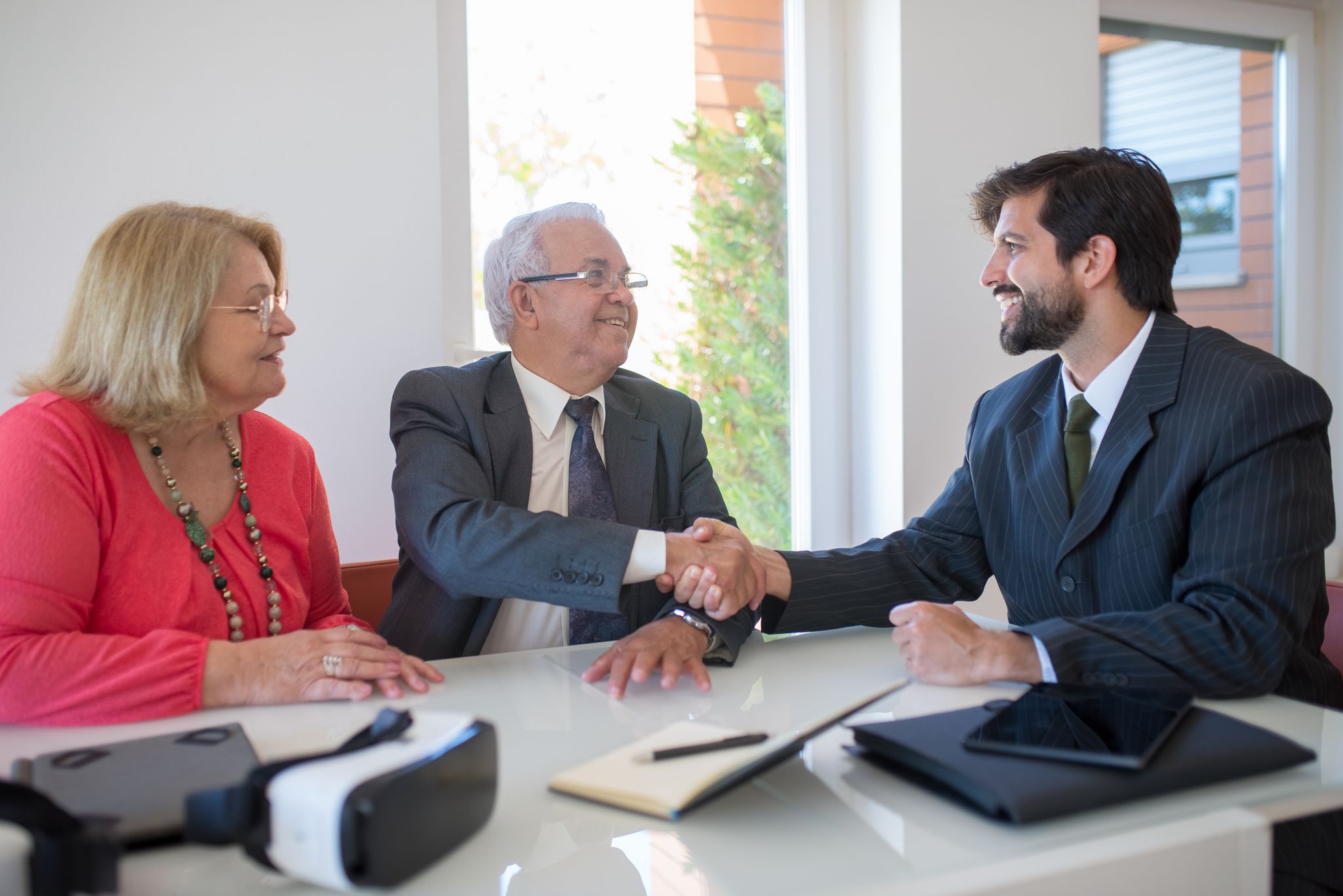 Three business professionals shaking hands during a meeting in an office, symbolizing successful deal-making.